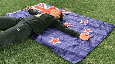 Theresa Fitzpatrick lying on the New Zealand flag on the grass looking very happy. 
