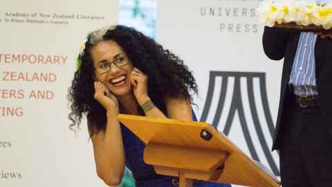 Selina Tusitala Marsh leaning over a lectern at a launch event for her poetry collection, leaning on her elbows and laughing.