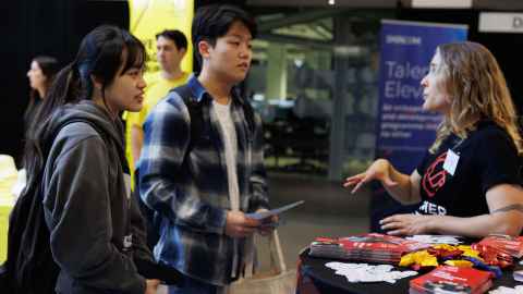 Two students standing at an employer stand talking to a woman who is an employment recruiter.