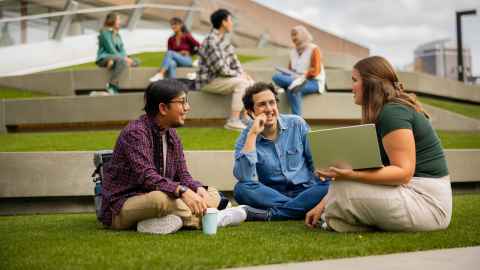 Group of students sitting on a grassed area on campus.