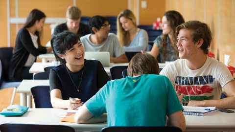 Group of students seated at a desk, laughing and working together.