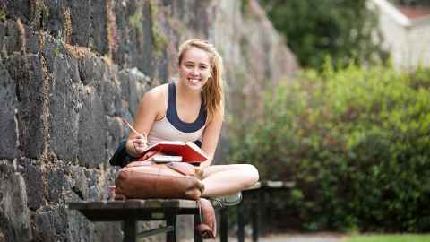Smiling woman sitting on seat outside studying.