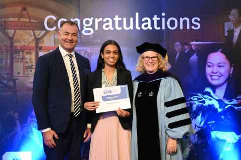 Three people standing by a 'Congratulations' sign and smiling