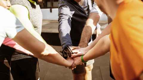 Photo of a group of people in a circle with their hands in the middle one on top of each other.