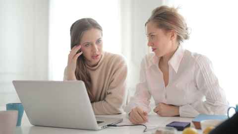 Photo of two people working at a desk laptop.