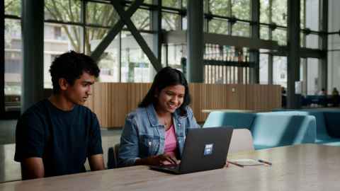 Students sitting at a desk looking at a laptop.