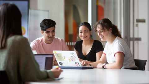 Group of smiling students looking at a laptop