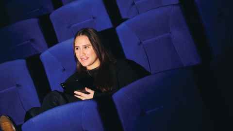 Student sitting in a row of blue chairs in a theatre.