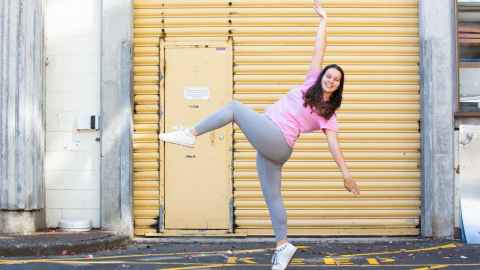 Dance student Maisie Dunning standing on one foot with one arm in the air, smiling