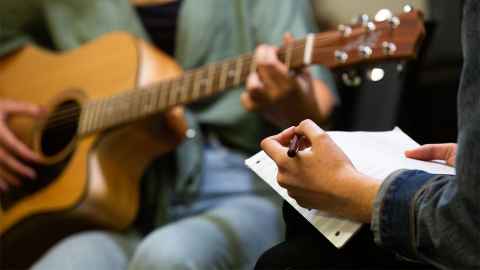 Students sitting together composing on guitar and using computer technology