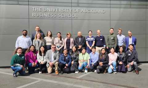 Group of people standing and sitting in front of the University of Auckland Business School.