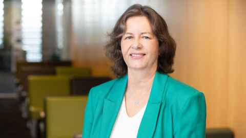 Image of a woman with brown, shoulder-length hair, wearing a green blazer and a white shirt, smiling.