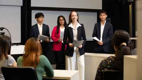 Group of four students standing at the front of a lecture theatre doing a presentation.