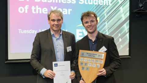 A smiling young man holding a shield-shaped wooden award alongside a smiling older man holding certificate