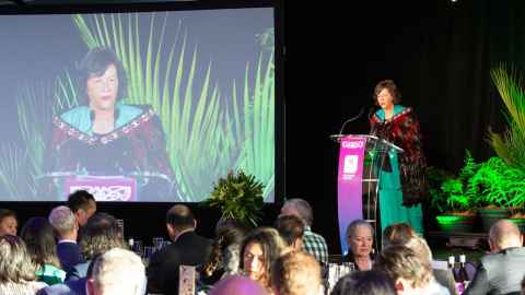 Image of Dean Susan Watson speaking on stage at the Aotearoa Maori Business Leaders Awards wearing a korowai.