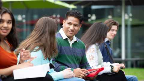 Five students sitting outside on the grass talking.