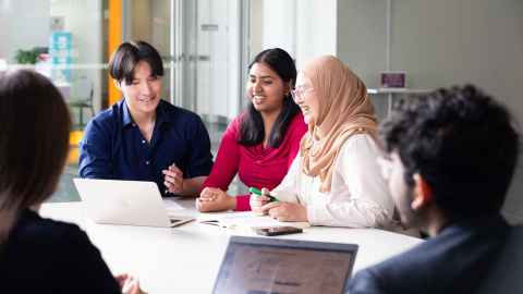 A group of students sitting at a table looking at laptops.