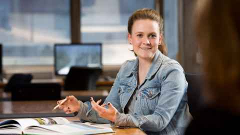 Person sitting at table, holding a pen. There is a textbook open in front of them.