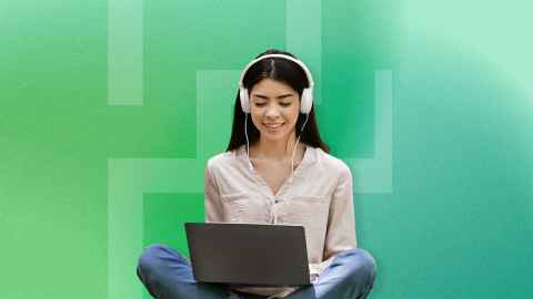 Girl sitting cross-legged with overhead headphones on smiling at a laptop that is open on her lap