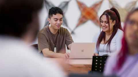 Two students sitting at a desk looking at a laptop together