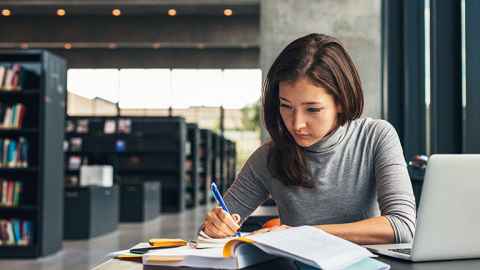 Student taking notes from a textbook in the library