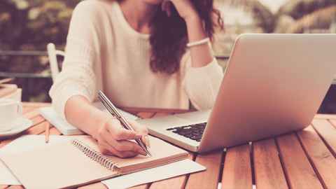 Woman working at a laptop and writing in a notebook