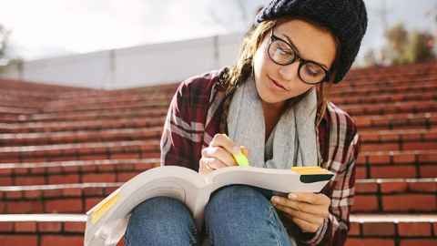 Girl sitting on steps highlighting things in a textbook