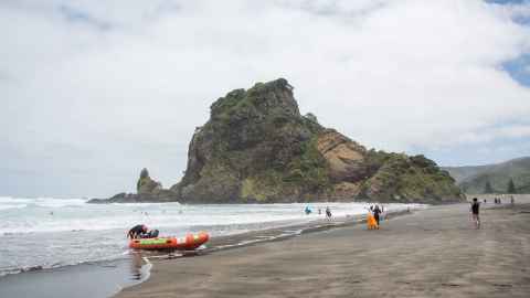 A surf life saving boat sits in the foreground of a scene at Piha Beach with swimmers in the water: While the drowning toll is heading in the right direction, New Zealanders must not get complacent. Photo: iStock
