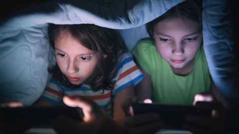 Kids playing video games on their devices hiding under a blanket