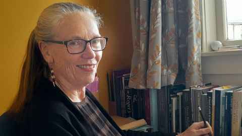 A portrait of Avril Bell in her office at her desk with books in the background.