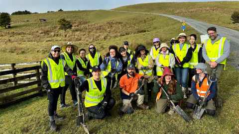 Close up of a group of smiling people in an outdoor rural setting wearing hi-vis vests and holding spades