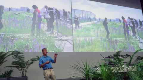 Dusty Gedge with a screen showing people working in the financial district in London as they explore an office's green rooftop. 