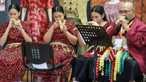 Three women and one man sitting down playing the nose flute in traditional Tongan dress.