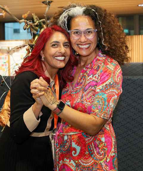 Professor Selina Tusitala Marsh and Associate Professor Rachael Jacobs wearing colourful clothes, smiling and holding hands as if they are dancing.