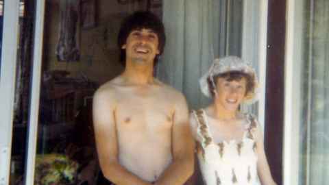 A young Julie and Carlo stand in a doorway. he is bare chested, she wears a summer dress and hat