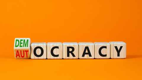 Row of wooden blocks spelling 'ocracy' with first block marked 'dem' or 'aut'