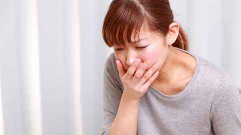 Young woman bending down and holding hand over mouth