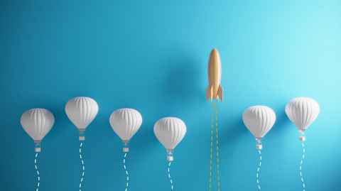 Image of rocket ascending, above a number of hot air balloons.