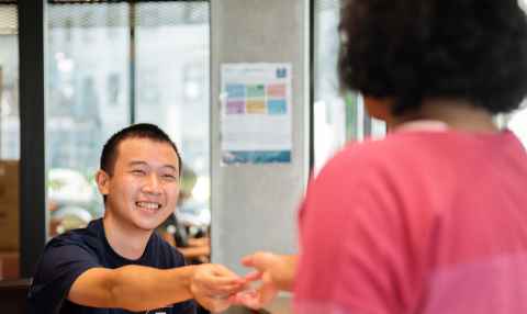 Resident is sitting a table looking up at an Accommodation staff member and speaking