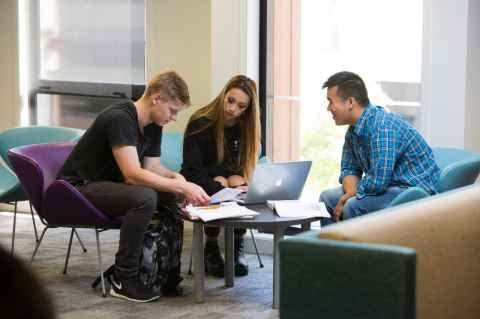 Three students sitting huddled around a laptop.