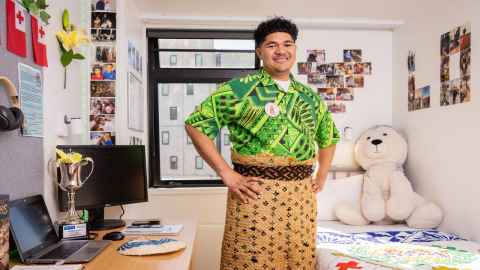 Lolo stands in his room with hands on his hips proudly wearing his ta'ovala. 