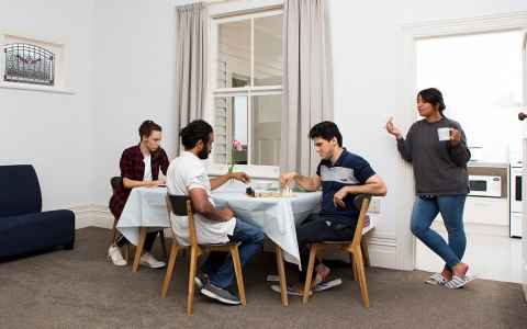 Group of four people in their flat around or near a table.