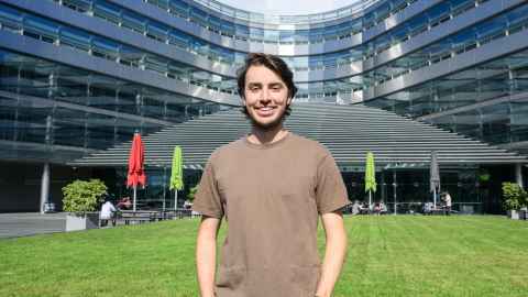 Man standing outdoors in front of a modern building and a grassy area