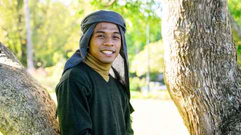 Man in traditional headress leaning against a tree